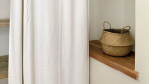 Una cortina blanca entreabierta, una cesta tejida sobre un estante de madera y suelo de madera.