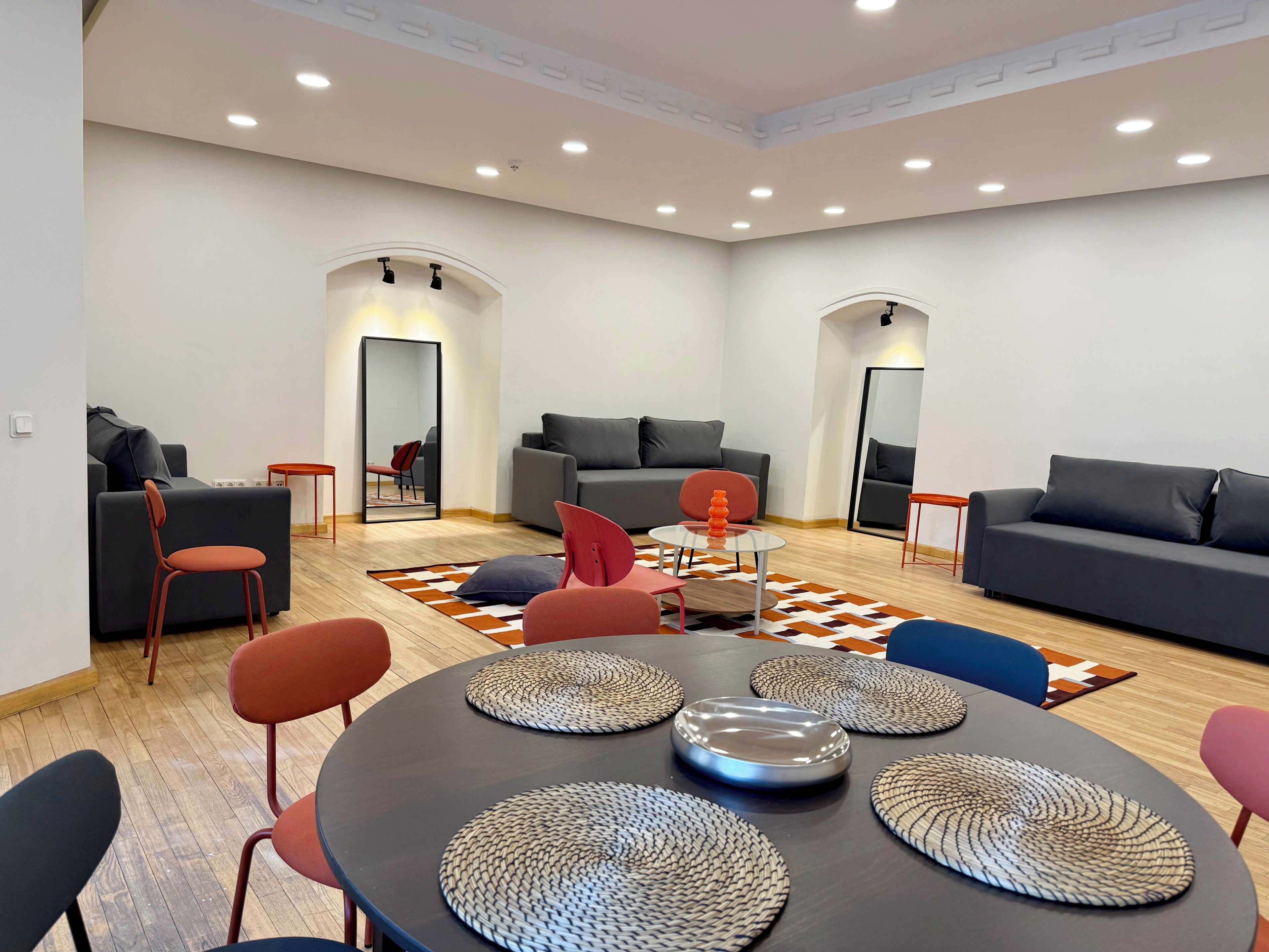 A modern living room with a round dining table, sofas, and a large mirror.