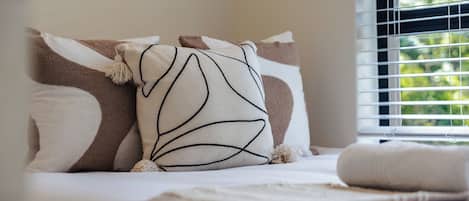 A bed with pillows and a blanket, a window with blinds, and a view of greenery outside.