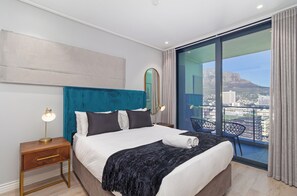 Une chambre d’hôtel avec un grand lit, une table de chevet, une chaise et une vue sur la ville grâce à de grandes fenêtres.