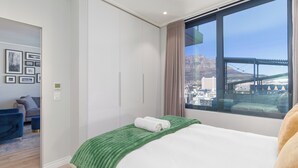 Hotellihuone, jossa on sänky, näköala kaupunkiin ja sillalle, vaatekaappi sekä oleskelualue, jossa on sohva ja nojatuoleja.