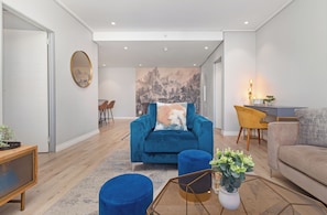 Ein modernes Wohnzimmer mit einem blauen Sessel, einem beigen Sofa und einem Couchtisch mit einer Pflanze.