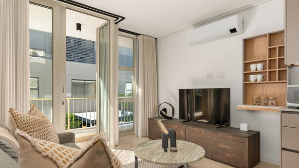A modern living room with a sofa, a glass coffee table, a TV, and a kitchen area with wooden cabinets and a microwave. - Designer Green Point Stay | Pool and Balcony (Cape Town)