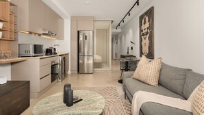 A modern living room with a grey sofa, a coffee table, and a kitchen area with appliances. - Designer Green Point Stay | Pool and Balcony (Cape Town)