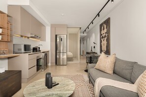 Ein modernes Wohnzimmer mit grauem Sofa, einem Couchtisch und einer Küchenzeile mit Geräten.
