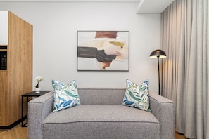 A modern living room with a grey sofa, two patterned throw pillows, a contemporary abstract painting, a floor lamp, and a wooden cabinet. - Apartment with Lake View | Balcony and Pool (Cape Town)