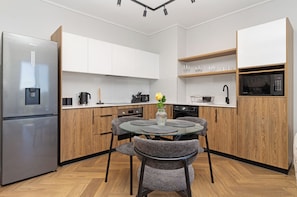 A modern kitchen with a stainless steel refrigerator, wooden cabinets, a dining table with chairs, and a microwave. - Apartment with Lake View | Balcony and Pool (Cape Town)