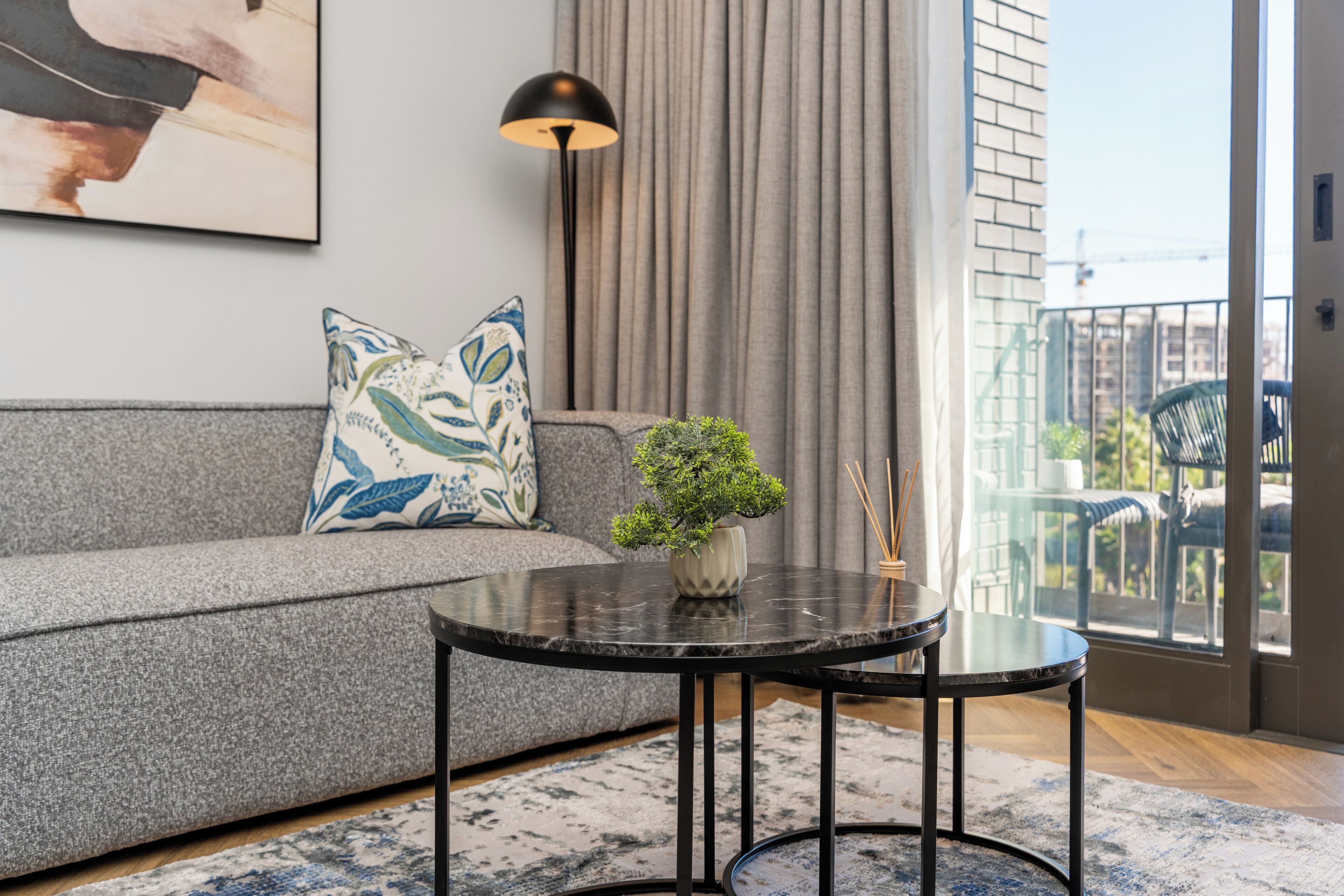 Een moderne woonkamer met een grijze bank, een ronde zwarte salontafel en een kleine potplant.
