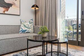 A modern living room with a grey sofa, a round black coffee table, and a small potted plant. - Apartment with Lake View | Balcony and Pool (Cape Town)