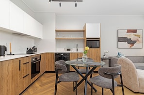 A modern kitchen with wooden cabinets, a dishwasher, and a dining area with a glass table and chairs. - Apartment with Lake View | Balcony and Pool (Cape Town)