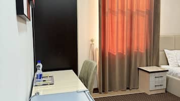 Quarto de hotel com escrivaninha, cadeira, cama, mesa de cabeceira e cortinas.