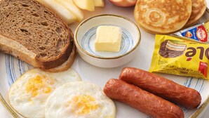 A breakfast plate with toast, eggs, sausages, a pomegranate, pancakes, and a packet of instant coffee. - Aral Hotel (Nukus)