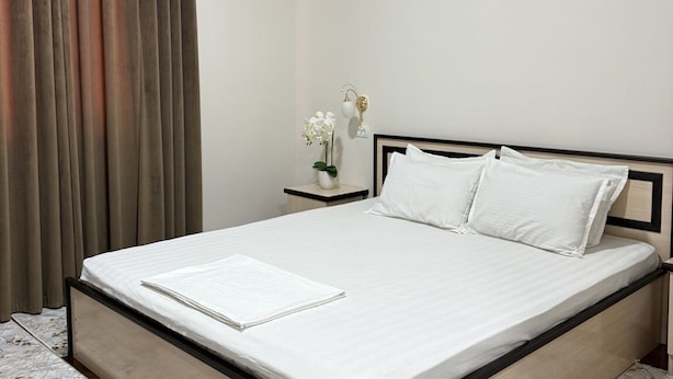 A neatly made bed with a white mattress and pillows, a bedside table with a vase of flowers, and a modern ceiling design. - Aral Hotel (Nukus)