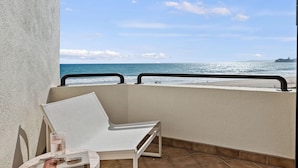 A balcony with a white chair, a small table, and a book. The balcony overlooks a beach with the ocean and a distant island. - Padaro by the Sea - Exclusive Beachfront Estate (Carpinteria)