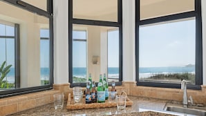 A kitchen with a granite countertop, a built-in dishwasher, and a view of the ocean through large windows. - Padaro by the Sea - Exclusive Beachfront Estate (Carpinteria)