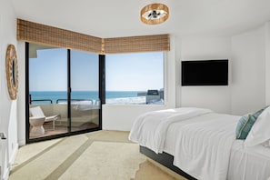 A bedroom with a bed, a TV, a view of the sea, and a balcony with a chair.