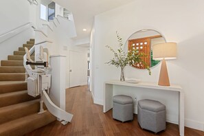 A modern interior with a spiral staircase, a console table with a mirror, and two ottomans.