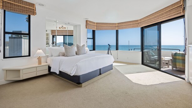A bedroom with a large bed, a nightstand, a lamp, a telescope, and a view of the ocean. - Padaro by the Sea - Exclusive Beachfront Estate (Carpinteria)