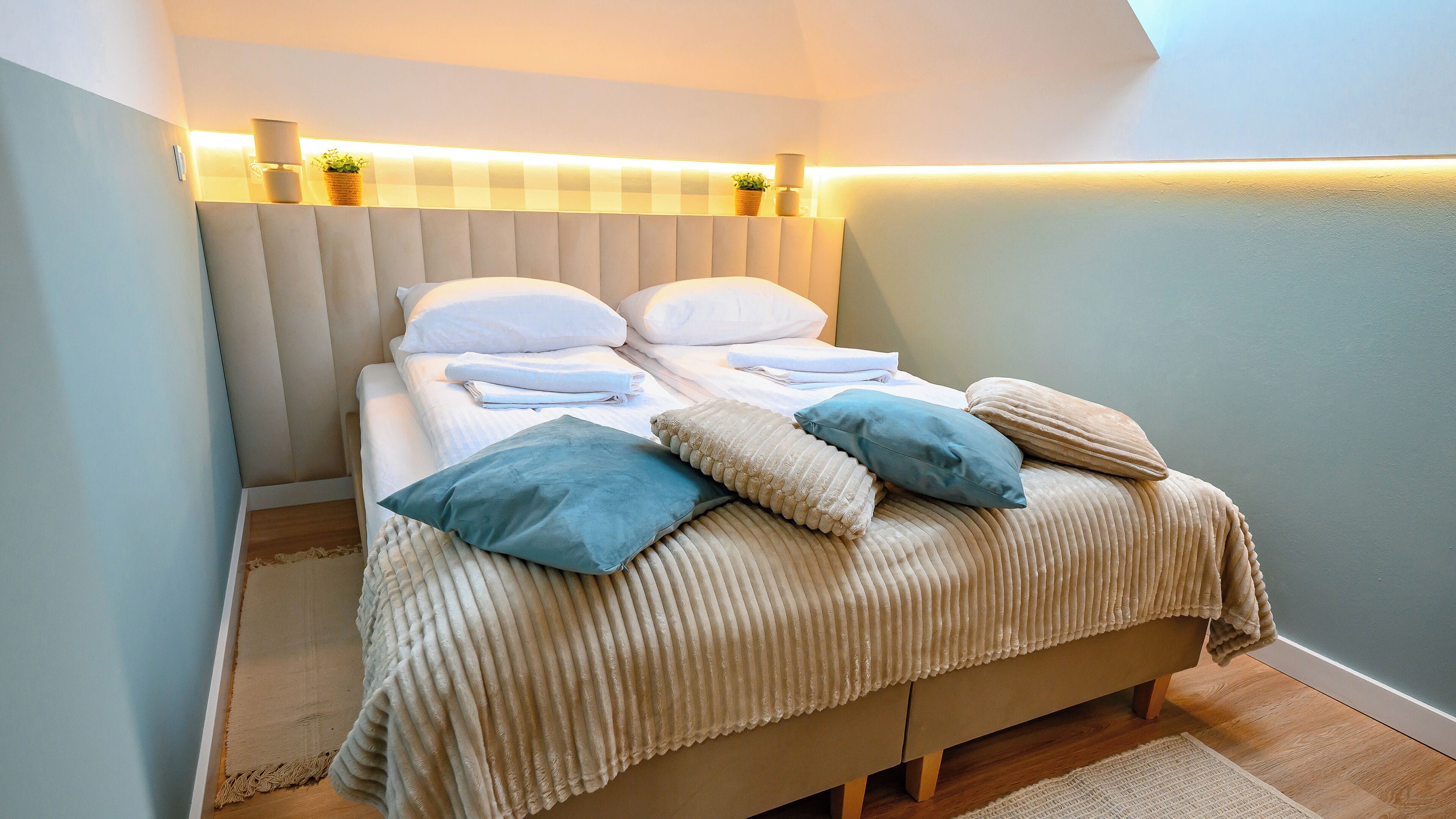 A neatly made bed with pillows and a blanket, a bedside lamp, and a wall-mounted shelf with a plant.