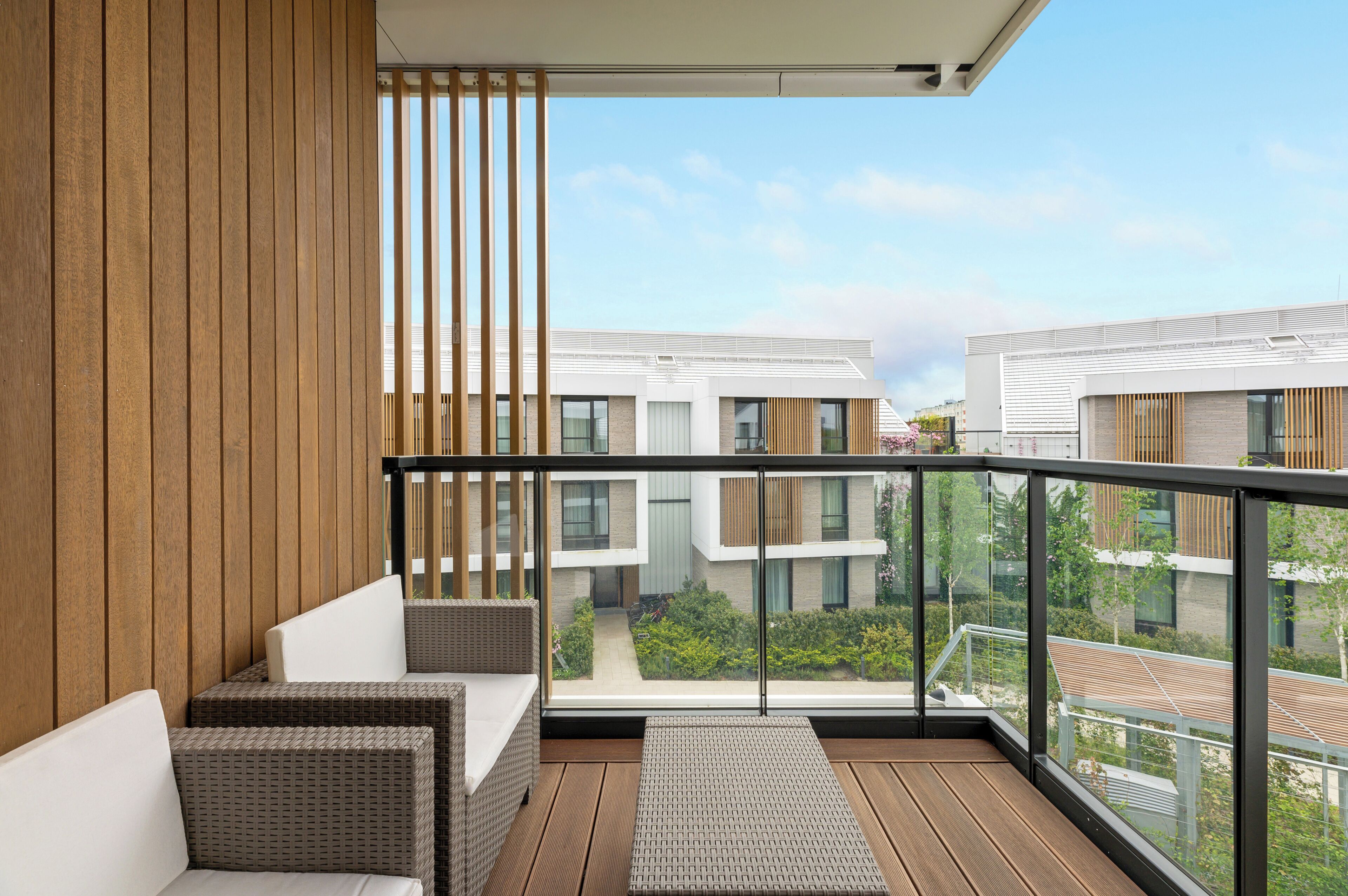 A balcony with wicker furniture, a view of a modern building complex, and a clear sky.