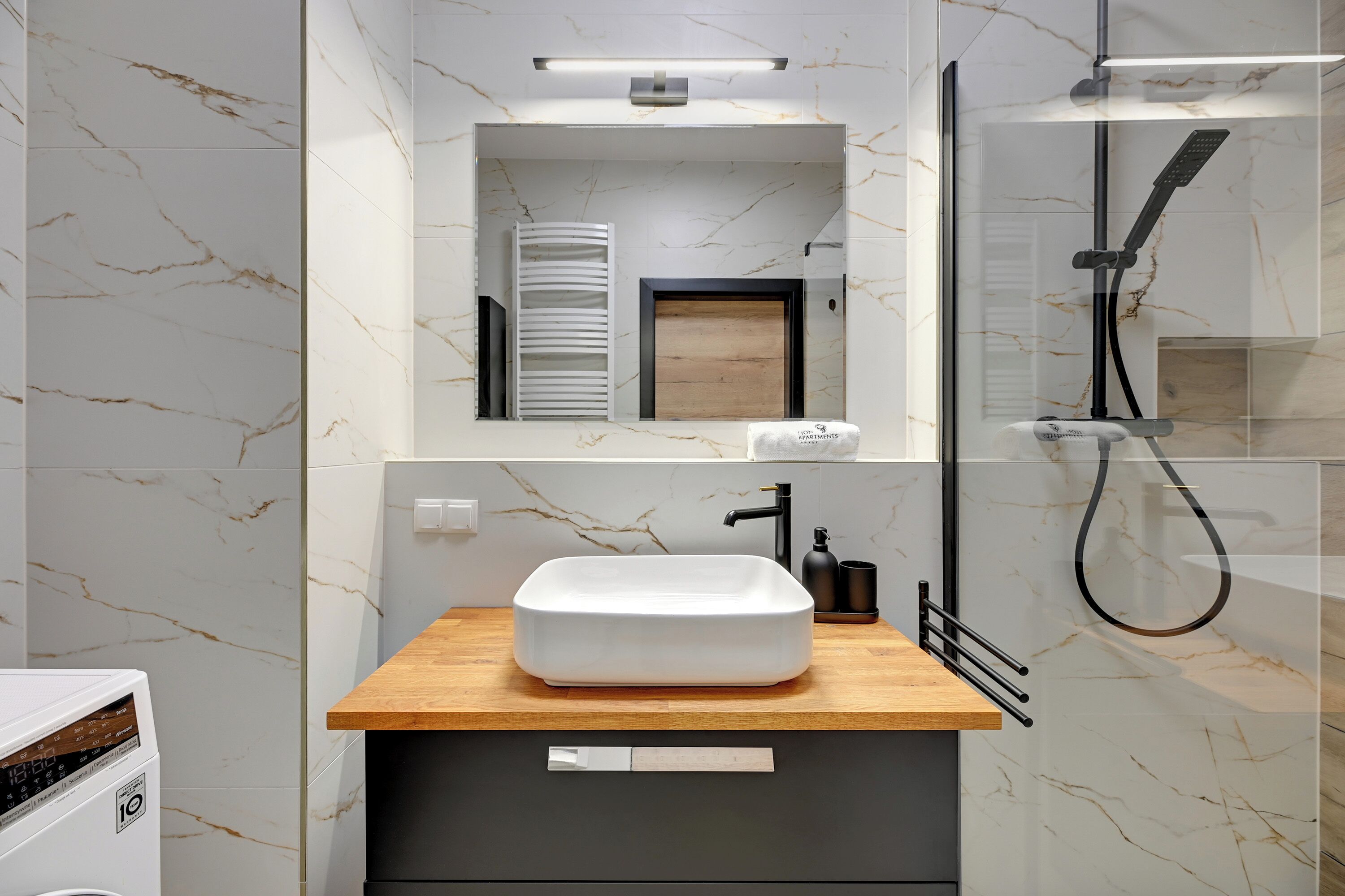 A modern bathroom with a marble backsplash, a wooden vanity, a white sink, a glass-enclosed shower, and a towel rack.