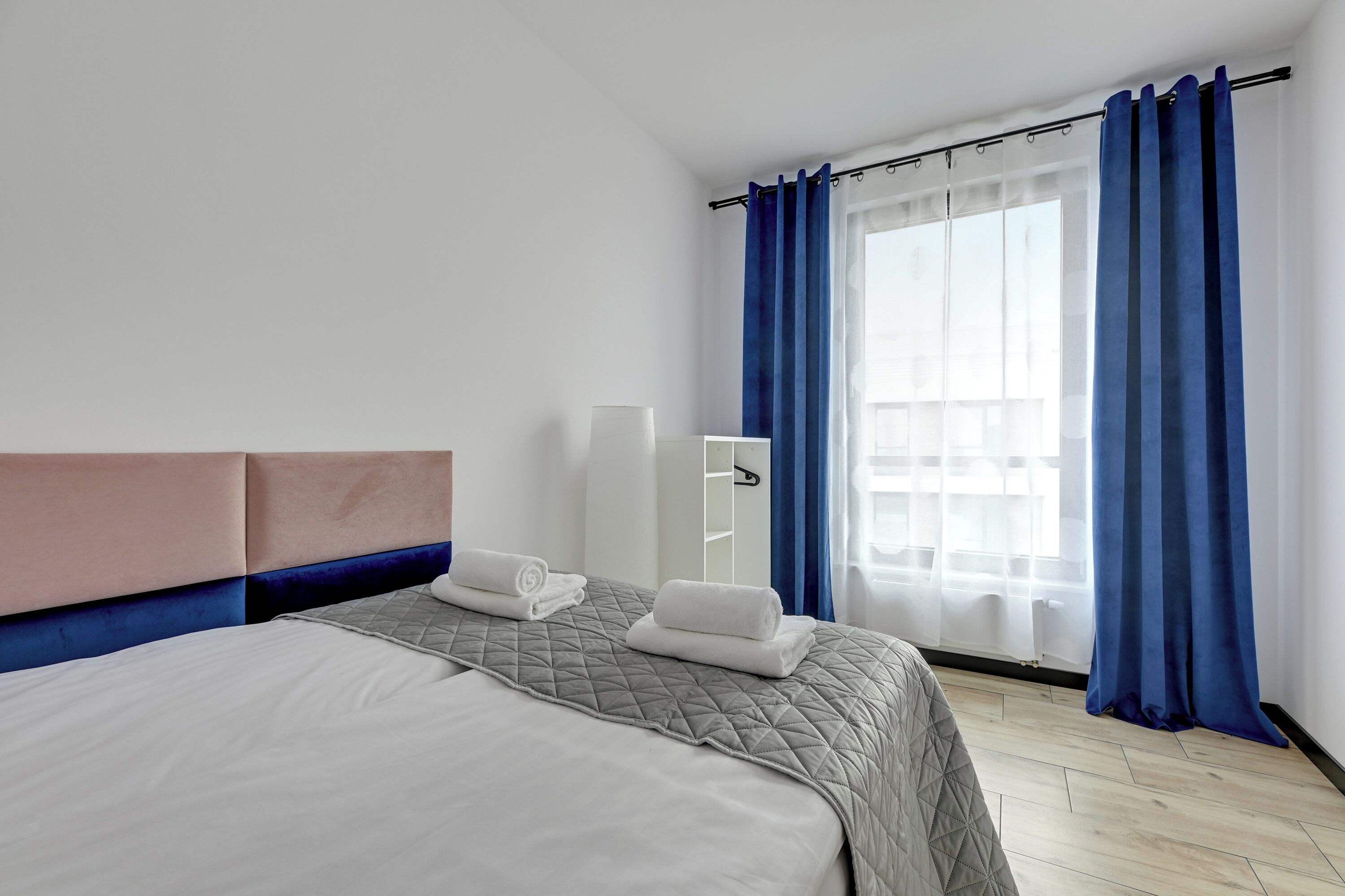 A hotel room with a bed, a bedside table, a mirror, and a window with curtains.