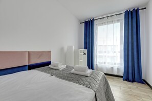 A hotel room with a bed, a bedside table, a mirror, and a window with curtains. - Botanica Jelitkowo Morze i Slow (Gdańsk)