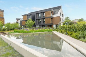 A modern residential building with a swimming pool, surrounded by lush greenery and purple flowers. - Botanica Jelitkowo Morze i Slow (Gdańsk)