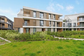 Um moderno edifício residencial com vários andares, varandas e um jardim bem cuidado.