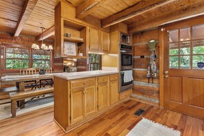 A rustic cabin-style kitchen with wooden cabinetry, a built-in oven, and a dining area with a bench.