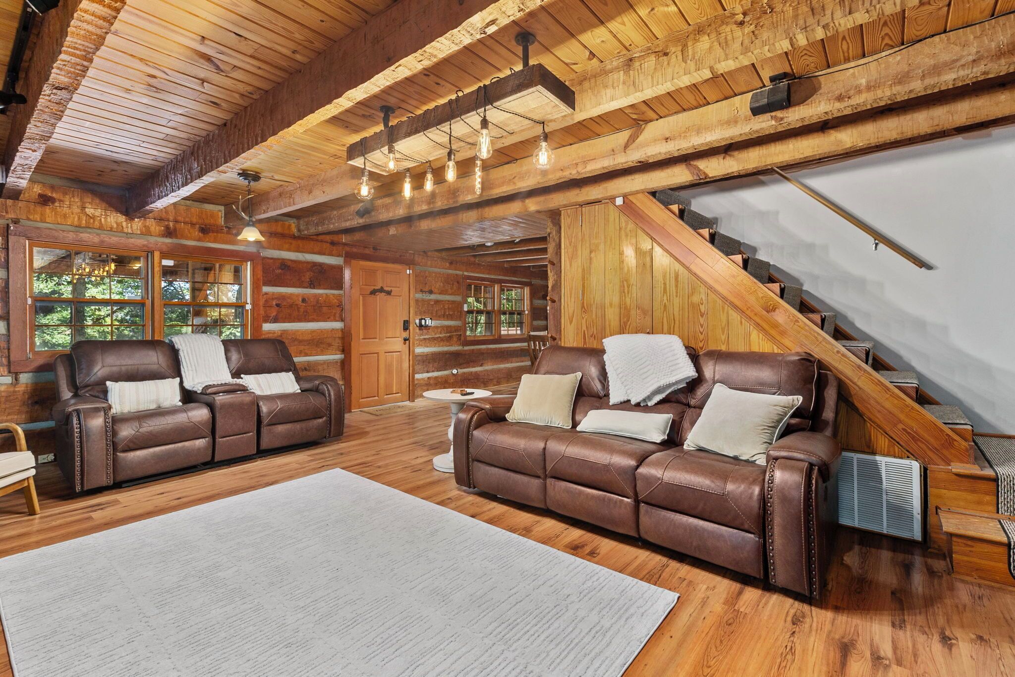 A log cabin interior with two leather sofas, a wooden staircase, and a large window.