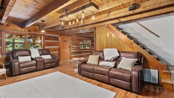 A log cabin interior with two leather sofas, a wooden staircase, and a large window.