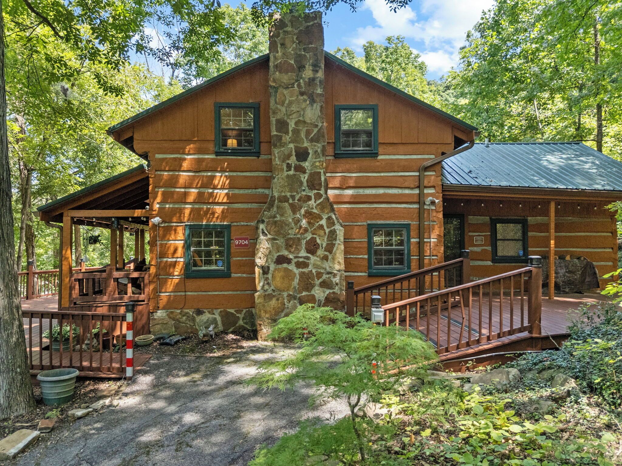 A log cabin with a stone chimney, wooden deck, and a stone foundation.