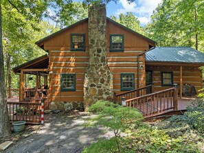 A log cabin with a stone chimney, wooden deck, and a stone foundation.
