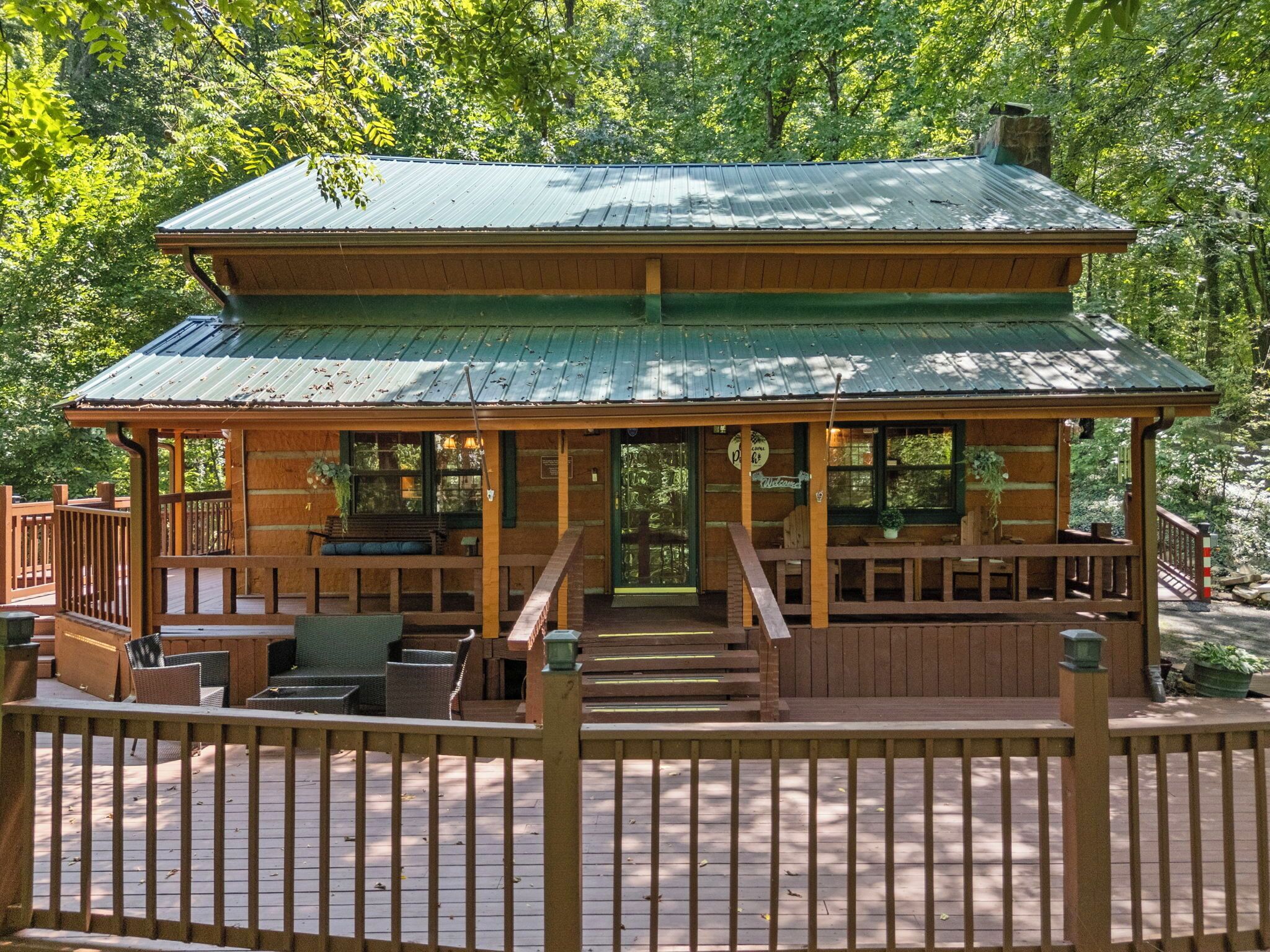 A wooden cabin with a covered deck, outdoor seating, and a staircase leading to the entrance.
