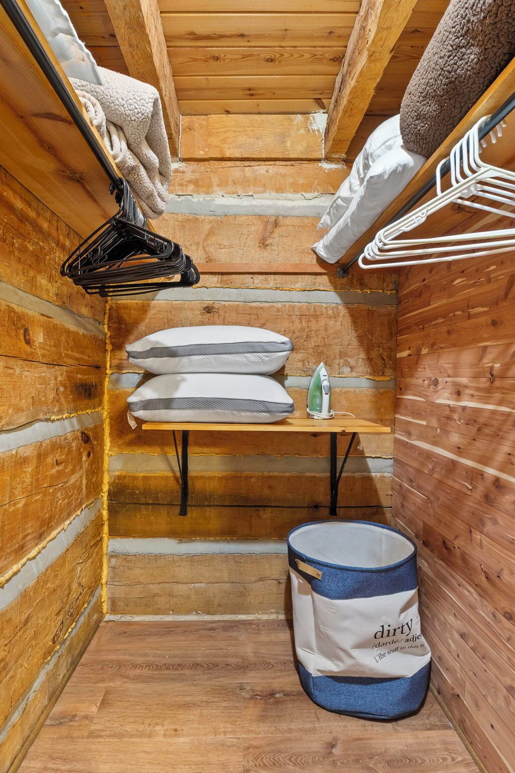 A small, wooden room with a wooden bench, a hanging clothes rack, and a storage bin.