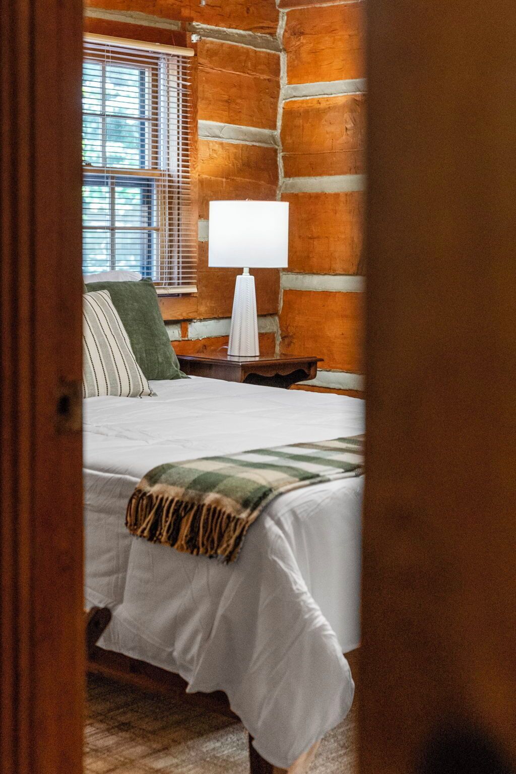 Une chambre à coucher avec un lit, une table de chevet, une lampe et une fenêtre avec des stores.