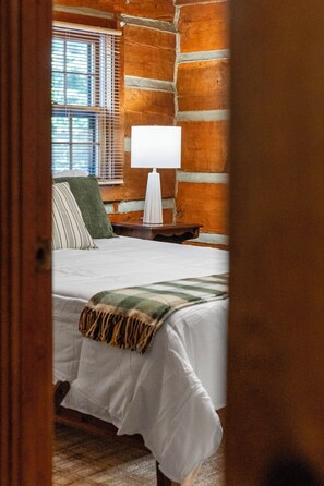Un dormitorio con cama, mesita de noche, lámpara y ventana con persianas.