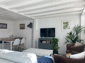 A modern living room with a flat-screen TV, a dining area with a table and chairs, a sofa, and a potted plant. - 'La Saucisserie' Walnut - 
Cozy cottage great for a small family or couple (Saint-Pierre-de-Frugie)