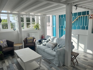A room with a white ceiling, a grey sofa, a white table, and a blue wall with geometric patterns. - 'La Saucisserie' Walnut - 
Cozy cottage great for a small family or couple (Saint-Pierre-de-Frugie)