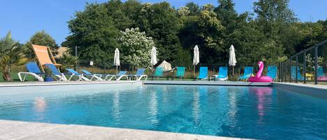 Une piscine entourée d’arbres, avec des chaises longues et des parasols.