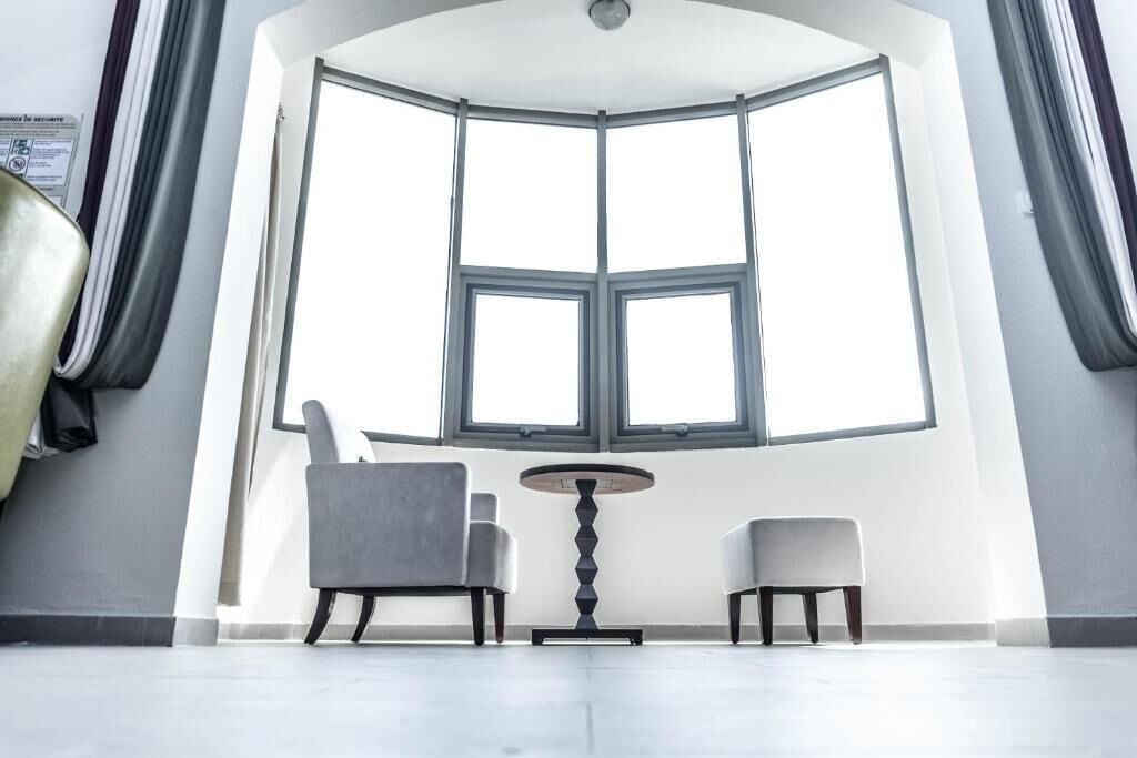Une pièce dotée d’une grande baie vitrée, de deux fauteuils, d’une petite table et d’un porte-manteau.