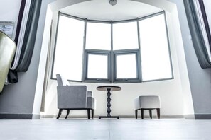 A room with a large bay window, two chairs, a small table, and a coat rack.