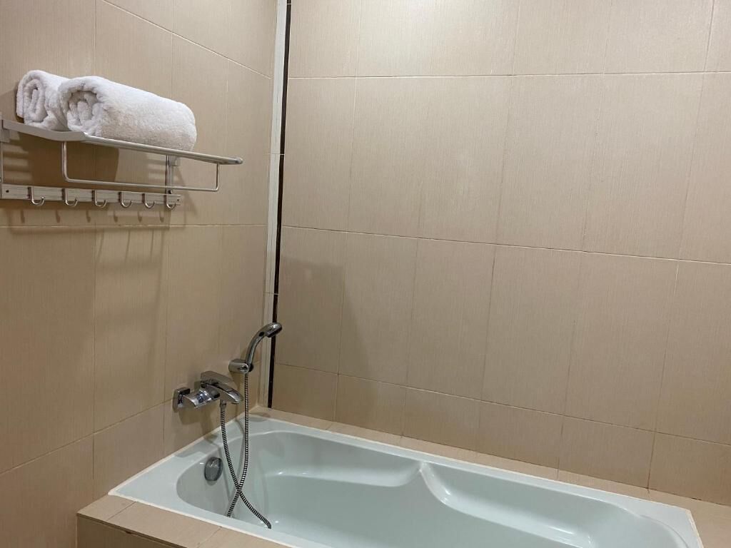 Et badeværelse med badekar, et håndklædetørrestativ med håndklæder og et brusehoved.