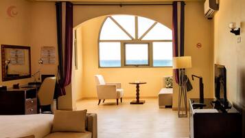 A hotel room with a bed, two armchairs, a small table, and a view of the sea through a large window.