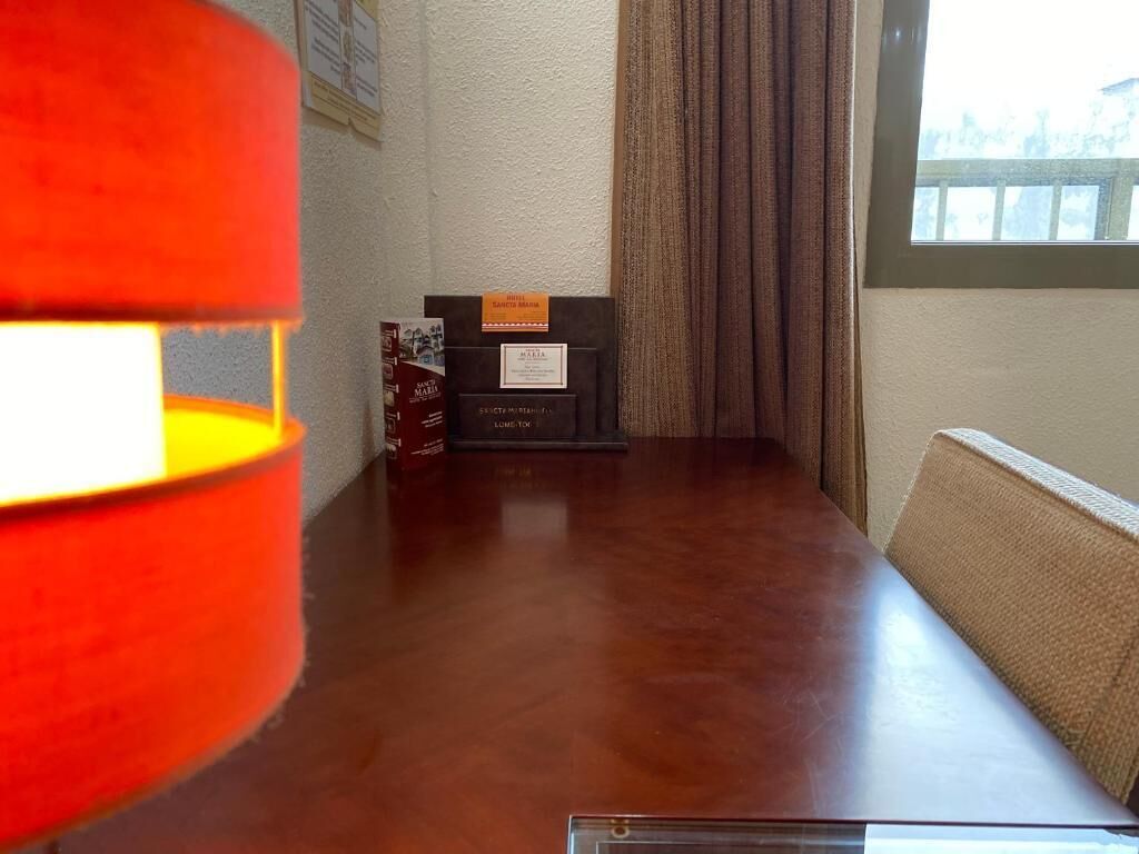 A wooden table with a plaque and a framed certificate, a window with curtains, and a sofa.