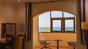 Habitación de hotel con ventanal curvo que ofrece vistas al mar, un escritorio con una silla y una pequeña mesa redonda.