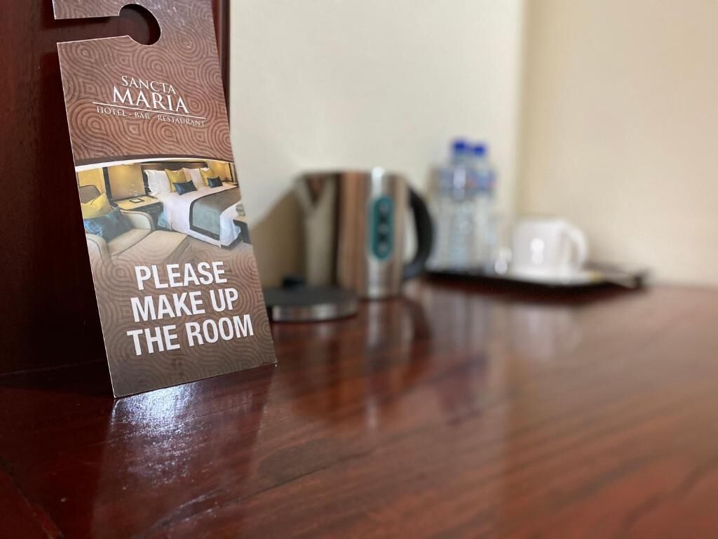 Schild in einem Hotelzimmer mit der Aufschrift 'Bitte Zimmer aufräumen', sowie ein Blick auf ein Bett und eine Kaffeemaschine.