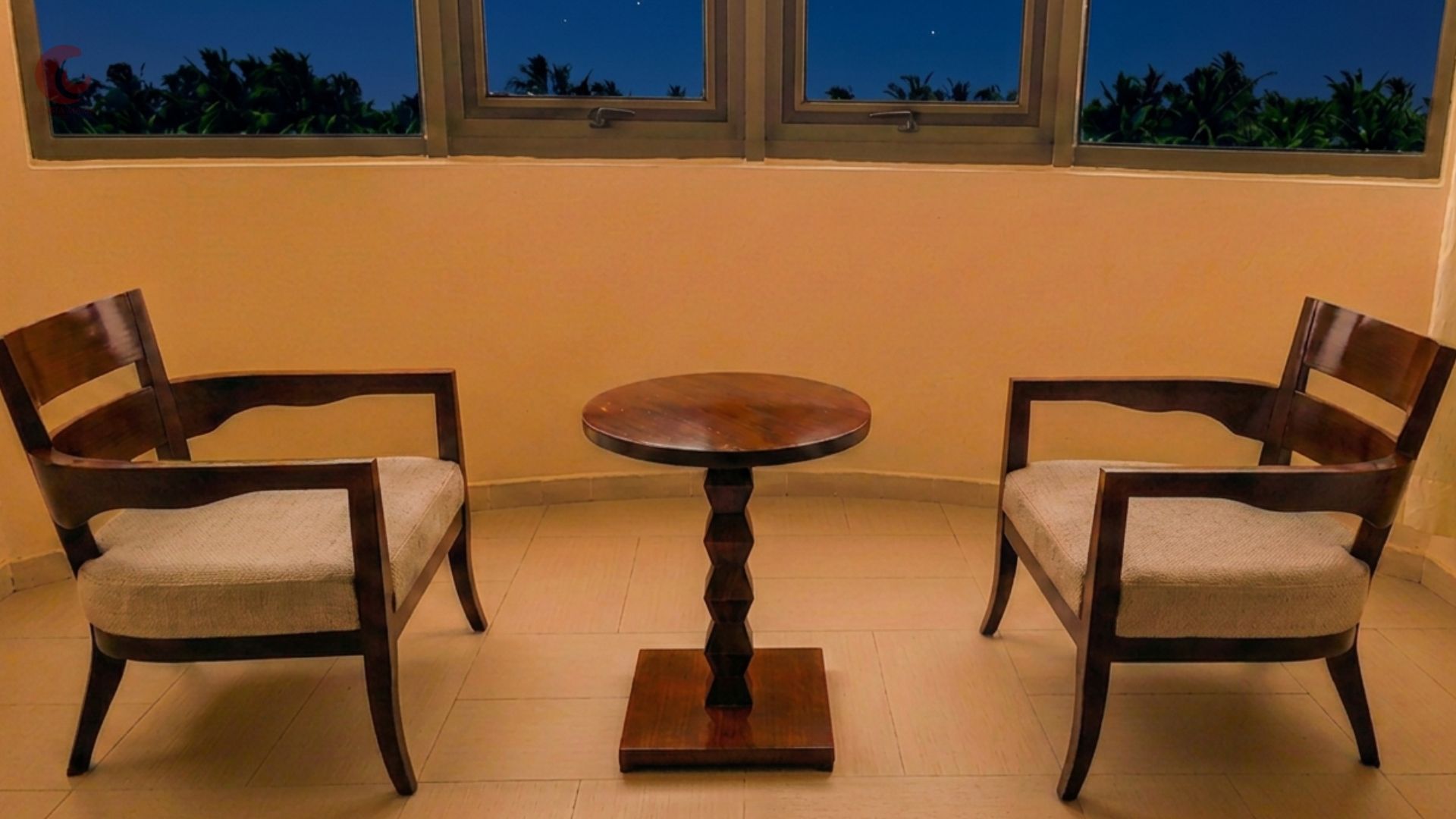 Une pièce avec deux chaises en bois et une table ronde, une fenêtre donnant sur le ciel nocturne et un sol carrelé.