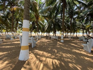 A beach area with white and yellow-striped palm trees, white benches, and a sandy ground. - Hôtel Sancta Maria  (Lomé)